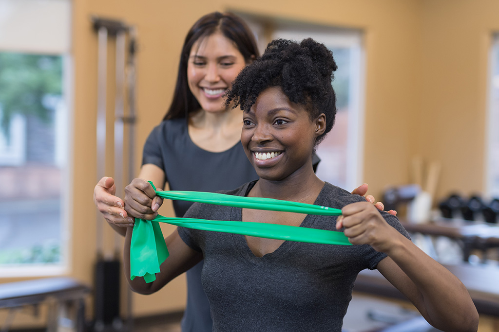 Two women, a physical therapist with patient, who is using a stretch band to build flexibility